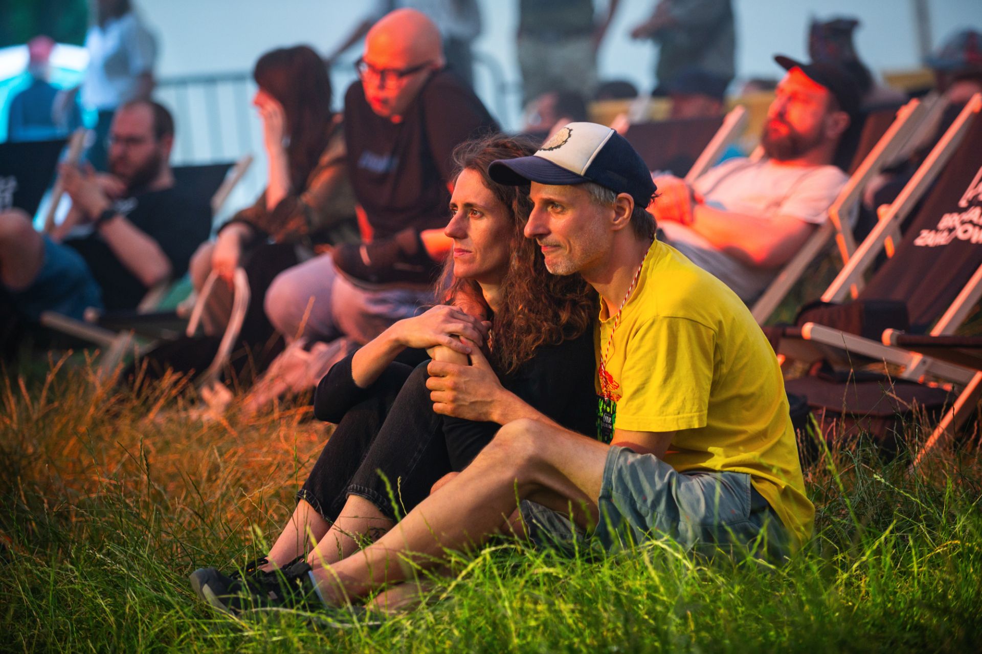 Kobieta i mężczyzna siedzą na trawie i słuchają koncertu.