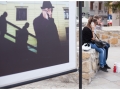 Ponownie zdjęcie z wystawy. Na pierwszym planie olbrzymia fotografia mieszcząca się na Placu po farze. Ukazuje ona mężczyznę oraz cienie dwóch osób. Obok fotografii siedzą młodzi ludzie.