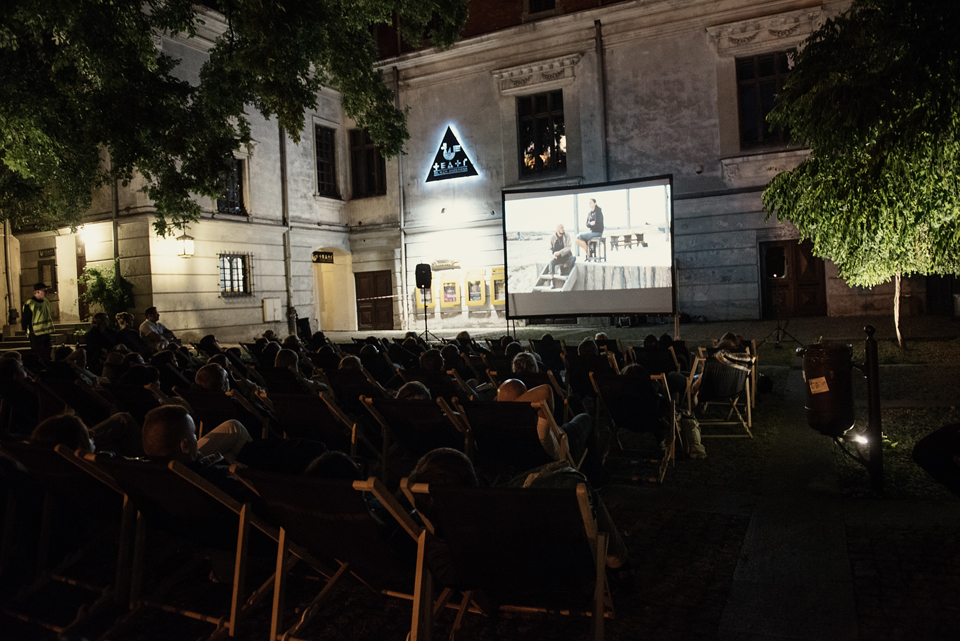 [Wydarzenie Movie East Movie. Plac przed Teatrem Hansa Christiana Andersena późnym wieczorem. Zebrani widzowie na leżakach oglądają film wyświetlony na dużym ekranie.]