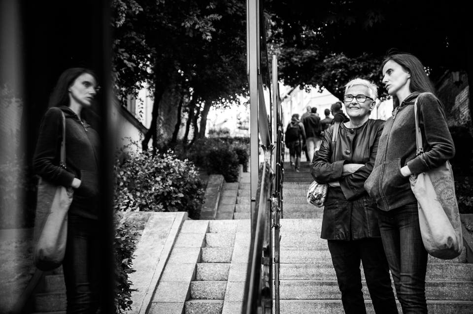 [Zdjęcie czarno-białe. Dwie kobiety oglądają wystawę umieszczoną w gablotach. Starsza kobieta uśmiecha się szeroko. Na twarzy młodszej kobiety widoczne zainteresowanie.]