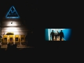 [Plac przed Teatrem Andersena. Wieczorny seans filmowy w ramach wydarzenia Move East Movie. Z lewej strony widoczne logo teatru, z prawej ekran z wyświetlanym filmem.]