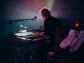 [Zdjęcie z koncertu. Skupiony mężczyzna gra na keyboardzie. Widok z boku. Niesamowite, klimatyczne oświetlenie sceny.]