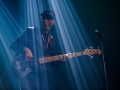 [Zdjęcie z koncertu Ayoub Houmanna & Nomads Moods. Mężczyzna w czarnej czapce z daszkiem gra na gitarze elektrycznej. Stoi w niebieskim oświetleniu.]