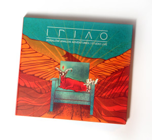 Okładka płyty zespołu Triao. Na niebieskim fotelu siedzi czerwony kozioł. Tło jest czerwono-niebieskie.