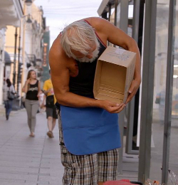 Starszy mężczyzna na ulicy pochyla się z pustym pudełkiem w kierunku chodnika.