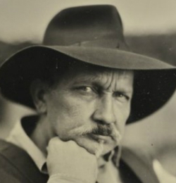 Fotografia czarno-biała, sprzed lat. Mężczyzna w kapeluszu podpiera się pod brodą.