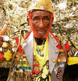Fotografia przedstawia Lee Perry'ego, jamajskiego producenta muzycznego. Ubrany jest w strój narodowy, ma pierścienie na palcach i żółtą czapkę na głowie. Broda pomalowana na czerwono.