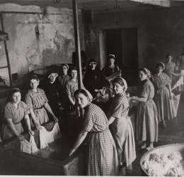 Zdjęcie czarno-białe, sprzed lat. Przedstawia kobiety piorące ubrania w wielkiej wannie.