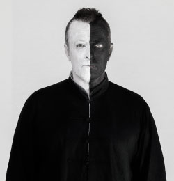 Czarno-biała fotografia muzyka o pseudonimie MU. Mężczyzna ma pomalowaną twarz: jedną połowę na biało, a drugą na czarno. Ubrany jest w ciemny sweter.